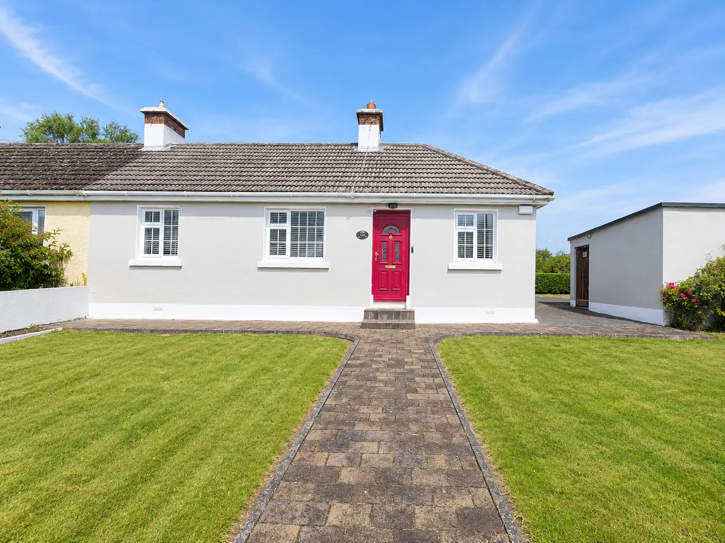 White bungalow with a red front door and neatly kept lawn at 14 Woodbrook, Mountrath